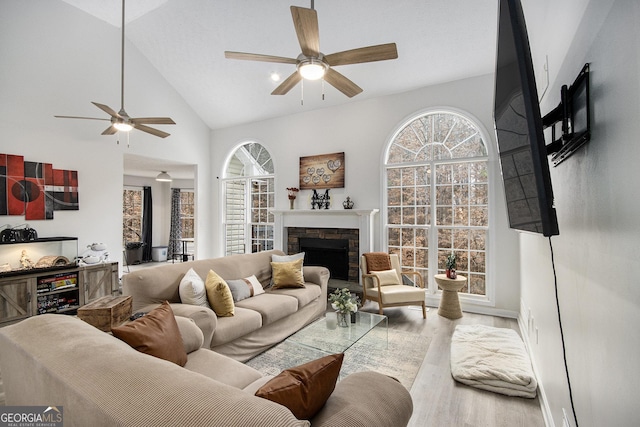 living room with ceiling fan, high vaulted ceiling, a fireplace, and light wood-type flooring