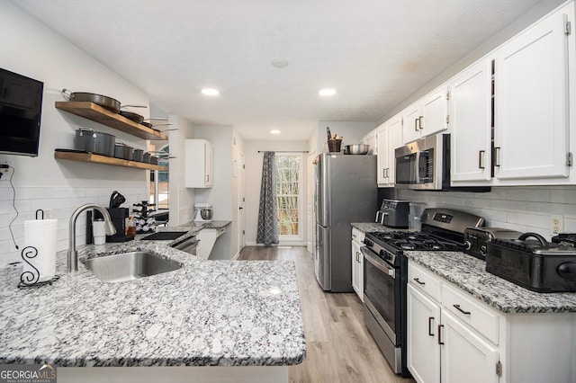 kitchen with sink, appliances with stainless steel finishes, white cabinetry, light stone countertops, and light wood-type flooring