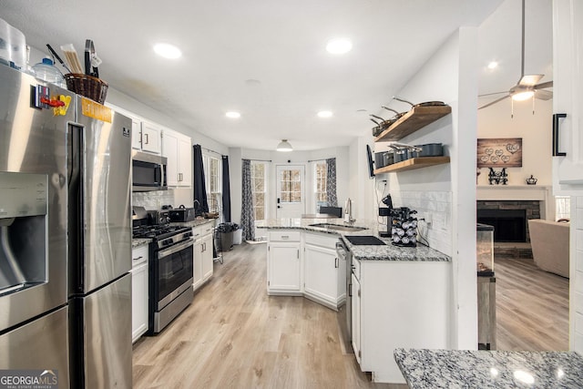 kitchen with sink, light stone counters, appliances with stainless steel finishes, kitchen peninsula, and white cabinets