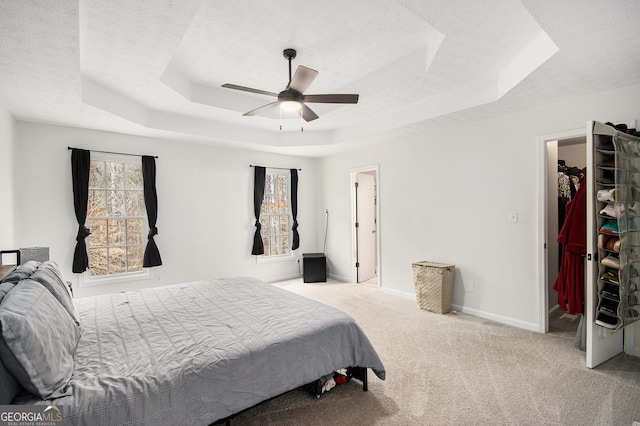 bedroom with a spacious closet, light colored carpet, a textured ceiling, and a tray ceiling