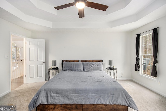 bedroom with light colored carpet, a raised ceiling, and ceiling fan