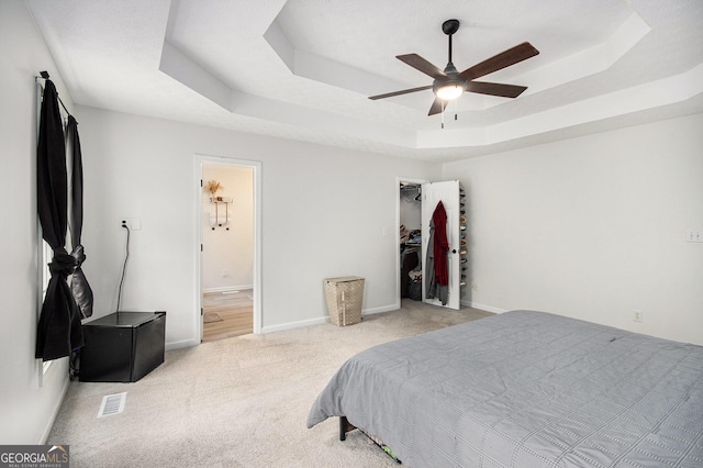 carpeted bedroom with ceiling fan, a walk in closet, connected bathroom, and a tray ceiling