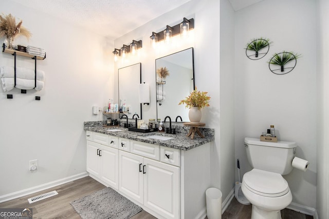 bathroom with hardwood / wood-style flooring, vanity, toilet, and a textured ceiling