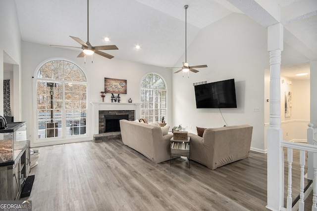 living room featuring light hardwood / wood-style flooring, ceiling fan, high vaulted ceiling, a fireplace, and ornate columns