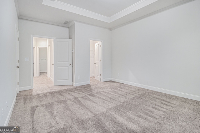 unfurnished bedroom with light colored carpet, ornamental molding, a raised ceiling, and ensuite bath