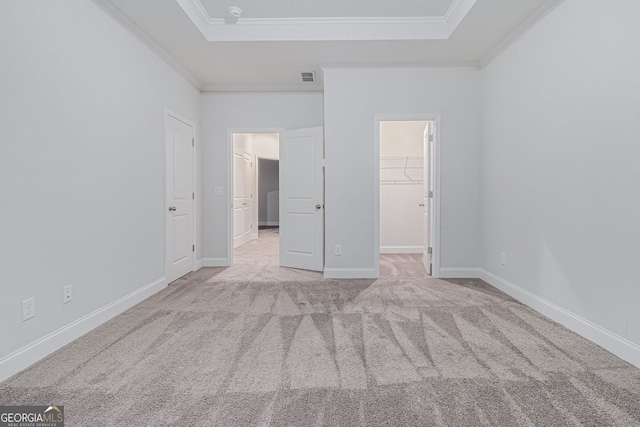 unfurnished bedroom featuring a spacious closet, light colored carpet, a tray ceiling, crown molding, and a closet