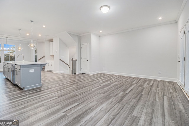 kitchen with sink, hanging light fixtures, ornamental molding, light hardwood / wood-style floors, and a center island with sink