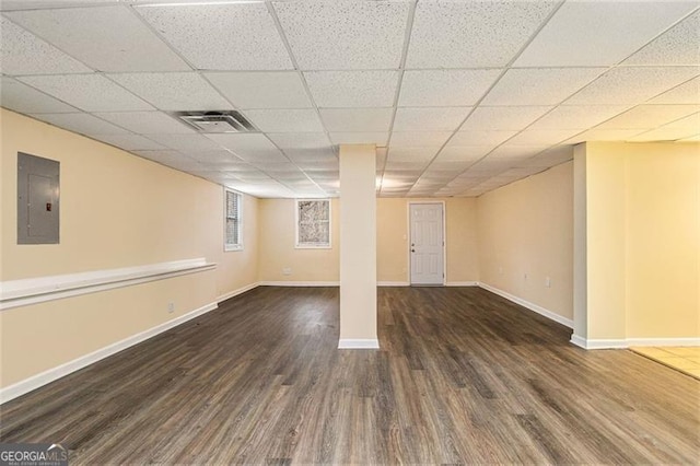 basement featuring a drop ceiling, electric panel, and dark hardwood / wood-style floors