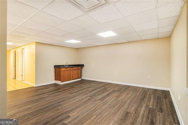 basement featuring sink, a paneled ceiling, and dark hardwood / wood-style floors