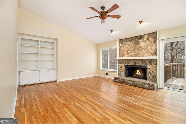 unfurnished living room featuring a stone fireplace, vaulted ceiling, ceiling fan, and light wood-type flooring