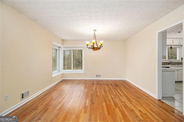 unfurnished dining area featuring an inviting chandelier, a wealth of natural light, a textured ceiling, and light hardwood / wood-style flooring