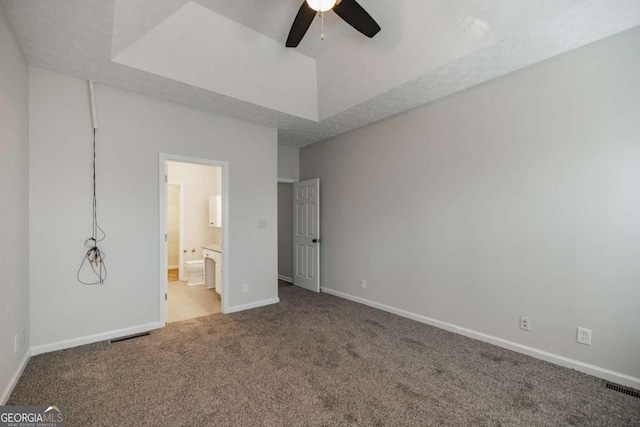 unfurnished bedroom with ensuite bath, ceiling fan, carpet, a textured ceiling, and a raised ceiling