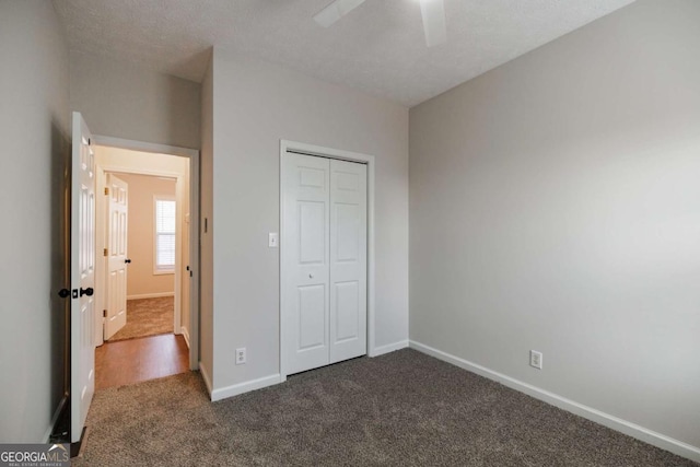 unfurnished bedroom featuring dark colored carpet, a textured ceiling, ceiling fan, and a closet