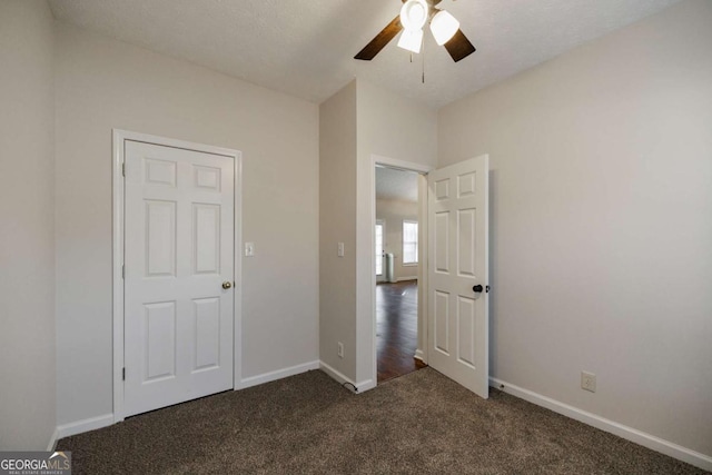 unfurnished bedroom with ceiling fan and dark colored carpet