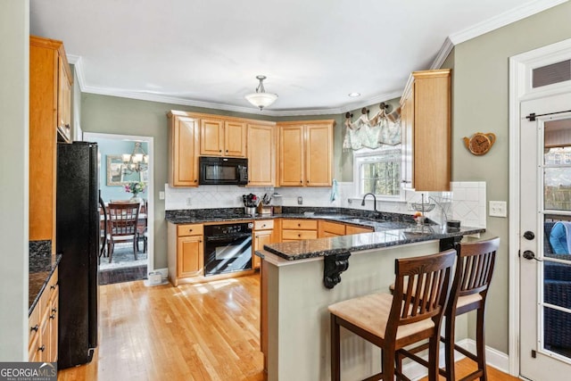 kitchen with sink, light wood-type flooring, kitchen peninsula, dark stone counters, and black appliances