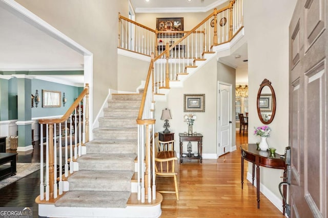 staircase featuring crown molding, wood-type flooring, and a high ceiling