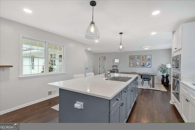 kitchen with appliances with stainless steel finishes, decorative light fixtures, a kitchen island with sink, and white cabinets