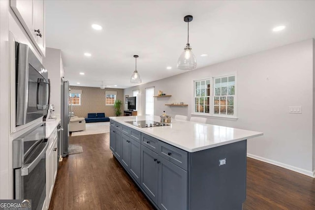 kitchen featuring dark wood-type flooring, appliances with stainless steel finishes, white cabinetry, a center island, and decorative light fixtures