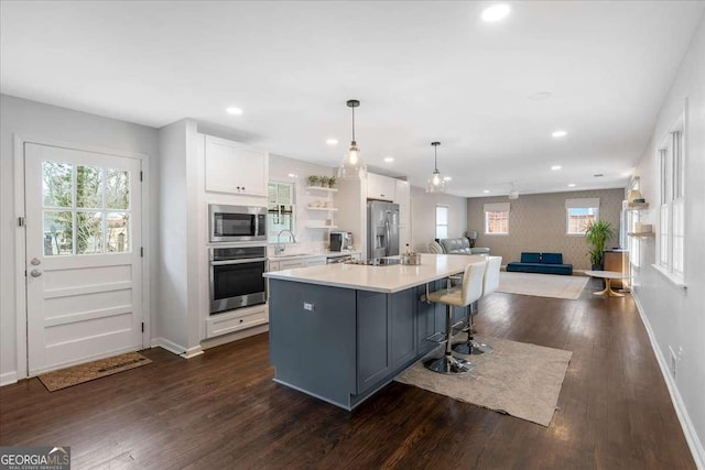 kitchen featuring sink, appliances with stainless steel finishes, a kitchen island with sink, hanging light fixtures, and white cabinets