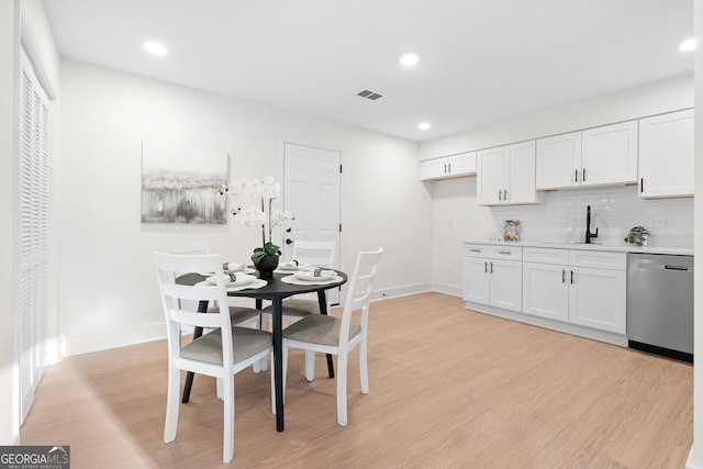 kitchen featuring white cabinetry, dishwasher, decorative backsplash, and light wood-type flooring