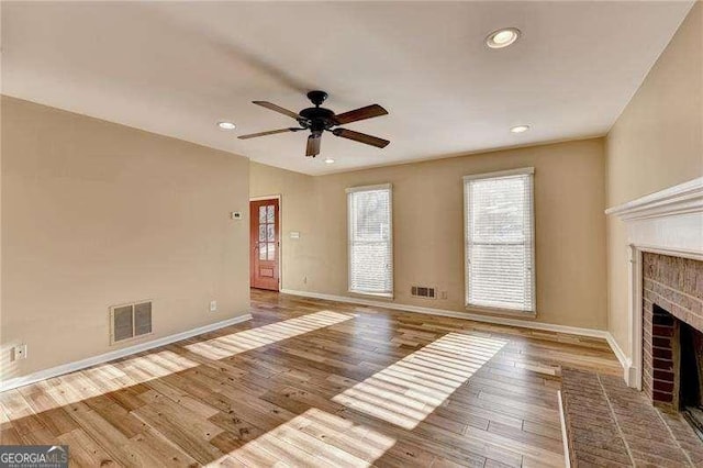 unfurnished living room featuring ceiling fan, hardwood / wood-style floors, and a brick fireplace