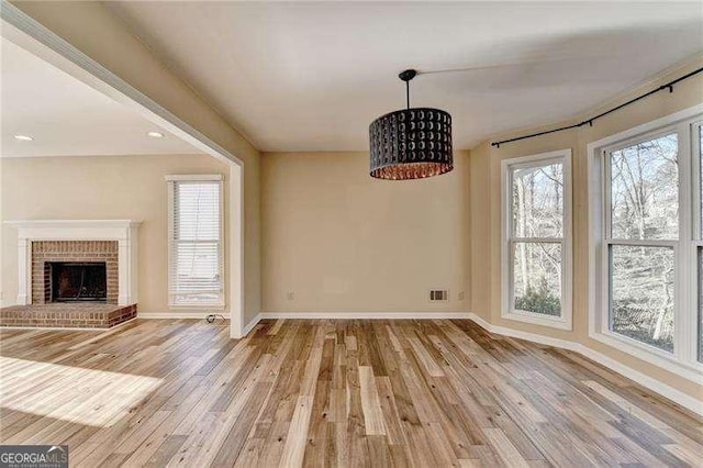 unfurnished dining area with a brick fireplace and light hardwood / wood-style floors