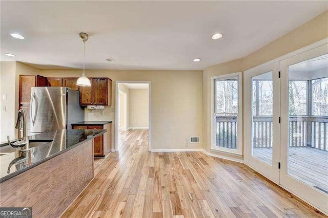 kitchen featuring pendant lighting, stainless steel refrigerator, sink, dark stone countertops, and light hardwood / wood-style floors