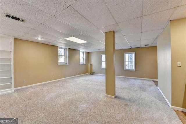 basement featuring a drop ceiling, plenty of natural light, and light carpet