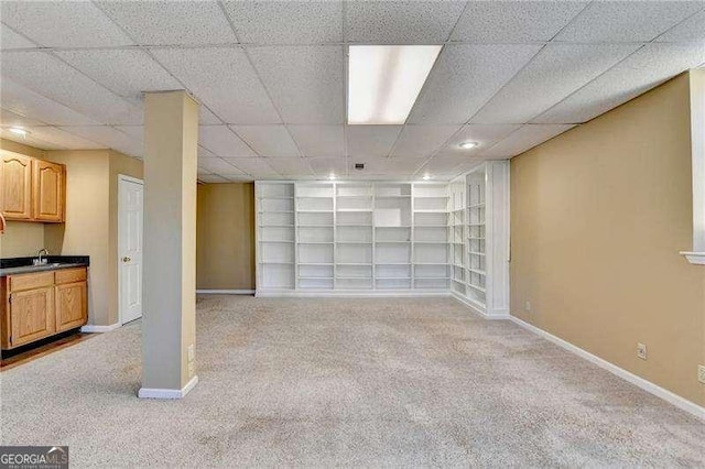 basement featuring light colored carpet, a paneled ceiling, sink, and built in features