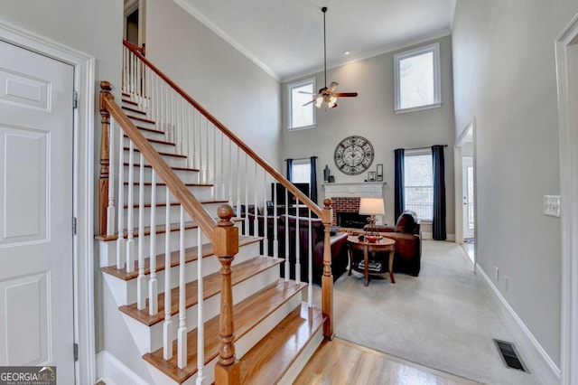 staircase with ceiling fan, crown molding, a fireplace, and a wealth of natural light