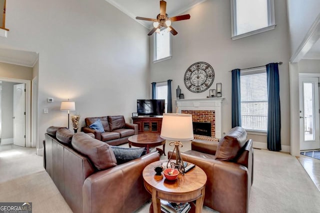 living room with light colored carpet, a brick fireplace, ornamental molding, a towering ceiling, and ceiling fan