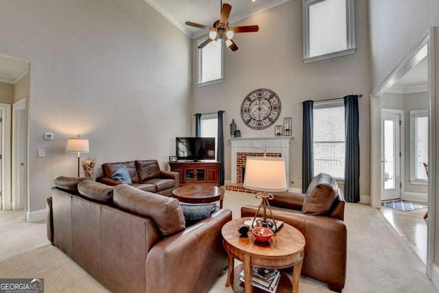 carpeted living room featuring a fireplace, ornamental molding, ceiling fan, and a high ceiling