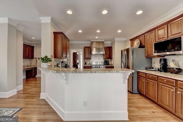 kitchen with appliances with stainless steel finishes, a breakfast bar, light stone counters, wall chimney range hood, and light wood-type flooring