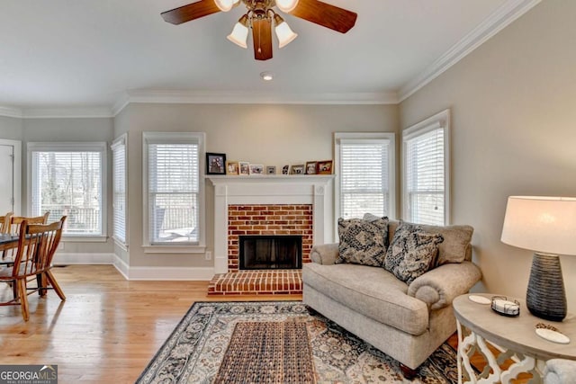 living room featuring ceiling fan, ornamental molding, a fireplace, and light hardwood / wood-style flooring