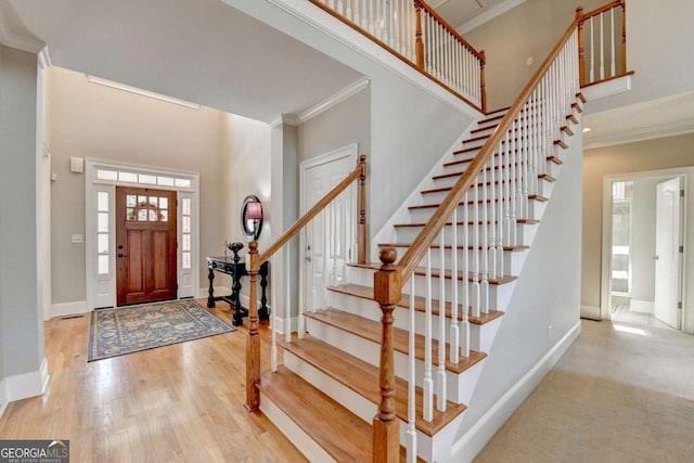 entryway with a towering ceiling, ornamental molding, and light wood-type flooring