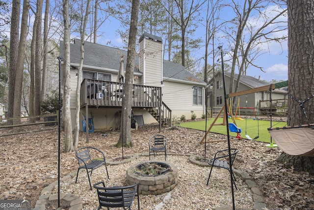 rear view of house with a fire pit, a lawn, a playground, and a deck