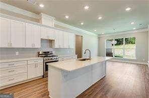 kitchen with stainless steel range oven, sink, crown molding, an island with sink, and white cabinets