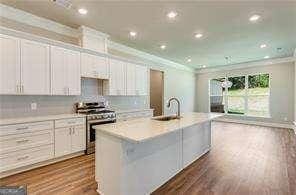 kitchen featuring crown molding, a sink, dark wood-type flooring, a kitchen island with sink, and stainless steel range oven