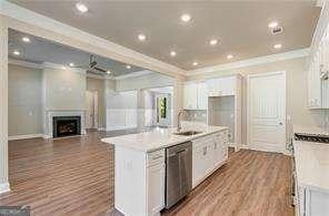 kitchen with an island with sink, light countertops, white cabinetry, stainless steel dishwasher, and ornamental molding