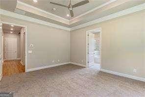 carpeted spare room featuring a raised ceiling, crown molding, baseboards, and ceiling fan
