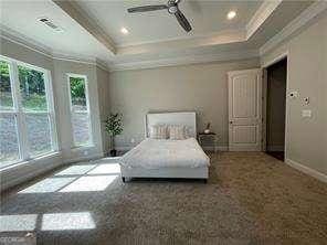 carpeted bedroom featuring a tray ceiling, multiple windows, and crown molding