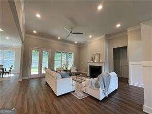 living area with a ceiling fan, dark wood-style floors, crown molding, and a fireplace