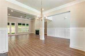 unfurnished living room with crown molding, a wainscoted wall, a decorative wall, a notable chandelier, and wood finished floors