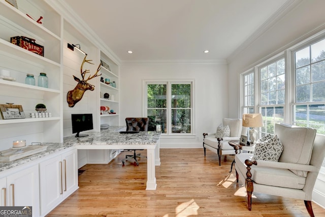 home office featuring crown molding, built in shelves, built in desk, and light hardwood / wood-style flooring