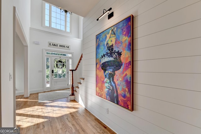 foyer entrance featuring a towering ceiling, light hardwood / wood-style floors, and wood walls