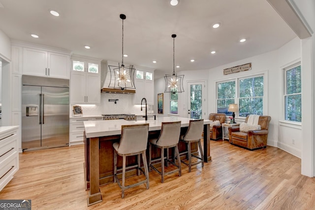 kitchen with white cabinetry, a center island with sink, light wood-type flooring, built in fridge, and decorative backsplash