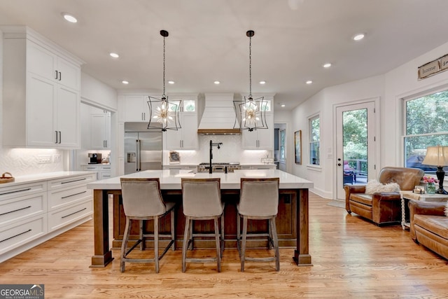 kitchen with pendant lighting, a chandelier, custom exhaust hood, a large island with sink, and built in refrigerator