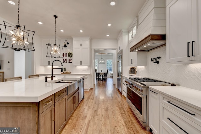 kitchen with pendant lighting, high quality appliances, white cabinetry, sink, and a kitchen island with sink