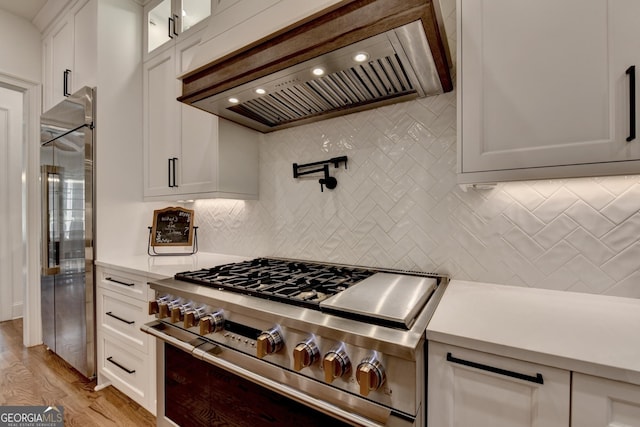 kitchen with premium range hood, backsplash, white cabinets, and premium appliances