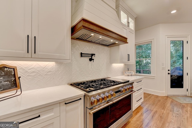 kitchen with tasteful backsplash, light hardwood / wood-style flooring, double oven range, custom range hood, and white cabinets